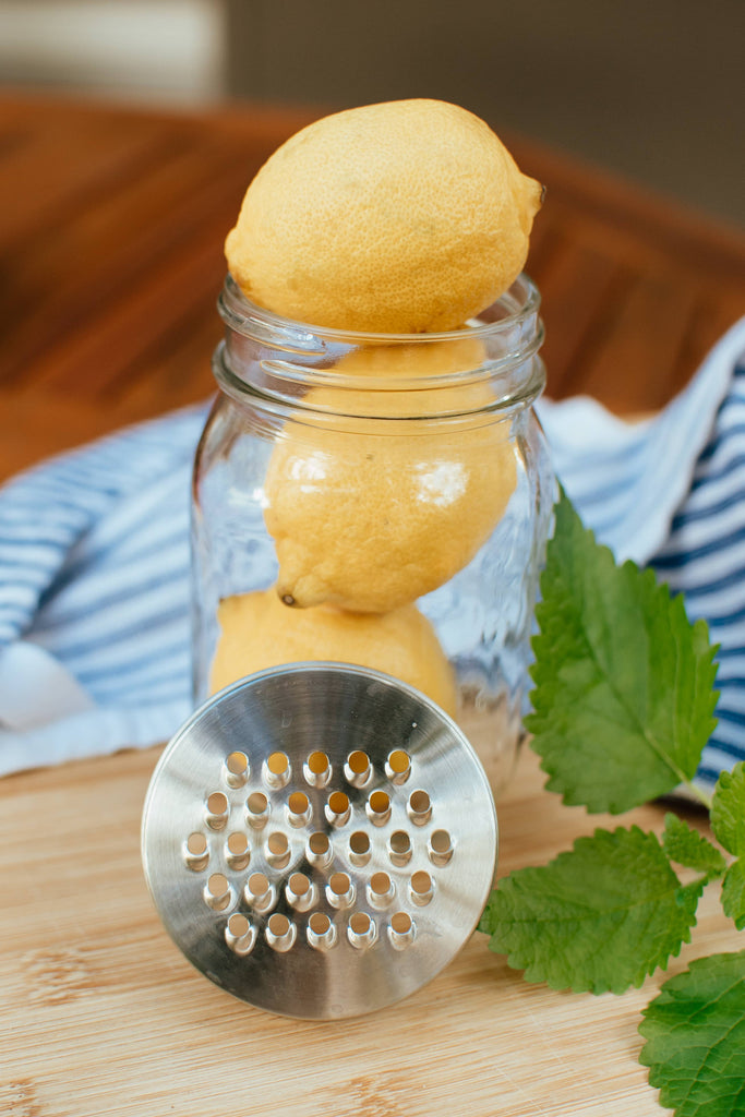 Glass jar with lemons and a metal grater on a wooden surface